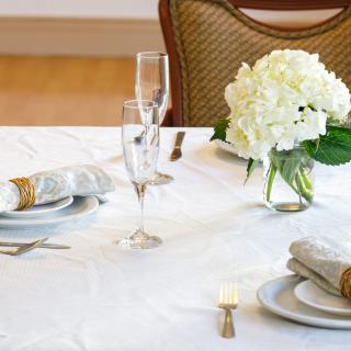 An elegantly set dining table with white hydrangea centerpiece, champagne glasses, and neatly arranged place settings.