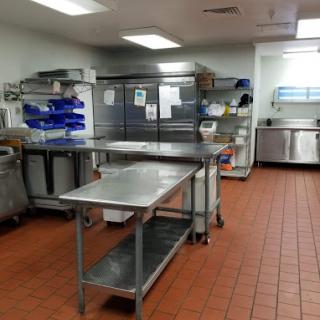 A well-organized commercial kitchen workspace, featuring stainless steel tables and storage units.