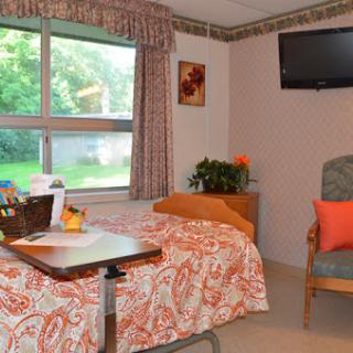 A cozy hospital room featuring a neatly made bed, a comfortable chair, and a view through the window.