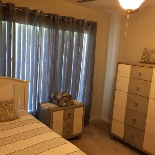 A cozy bedroom featuring a bed, dresser, and curtains.