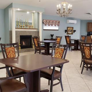 A cozy dining area with neatly arranged tables and chairs, featuring a fireplace and decorative chandelier.