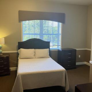 A cozy bedroom with a bed, two dressers, and a window letting in natural light.