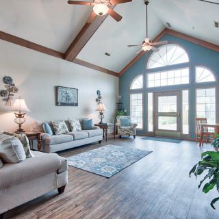 A spacious living room with vaulted ceiling, featuring comfortable sofas, a rug, and large windows letting in natural light.