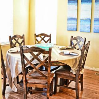 A cozy dining area featuring a round wooden table with six matching chairs, adorned with a simple tablecloth.