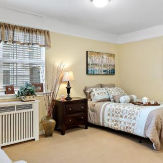 A cozy bedroom with a neatly made bed, a nightstand with a lamp, and tasteful wall decor.