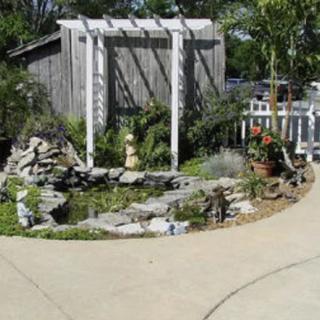 A beautifully landscaped garden featuring a pergola, pond, and stone pathway.