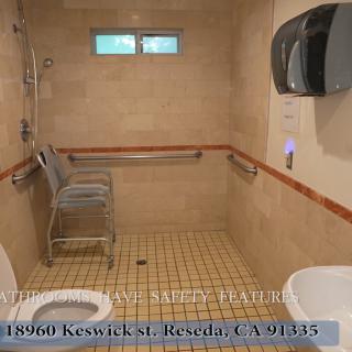 An accessible bathroom with a shower, toilet, sink, grab bars, and a paper towel dispenser.