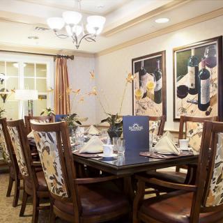 A well-decorated dining room featuring a set of elegant chairs and table, illuminated by a chandelier, with wine-themed paintings on the walls.