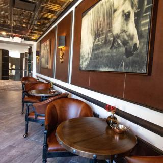 A cozy cafe interior featuring leather chairs, wooden tables, and horse-themed artwork on the walls.