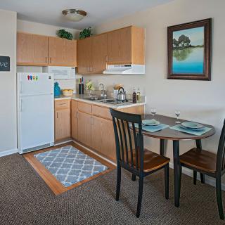 A cozy apartment kitchen with a dining area, featuring wooden cabinets and a small table with chairs.