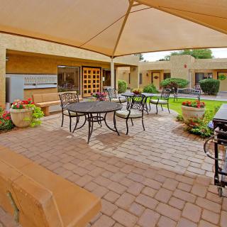 A cozy outdoor patio featuring a shaded seating area with metal furniture surrounded by a well-maintained garden.