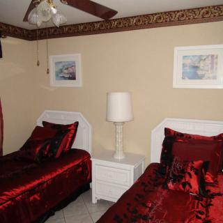 A cozy bedroom featuring twin beds with red bedding, a central lamp, and framed artwork on the walls.