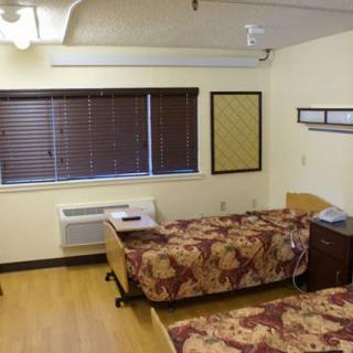 A hospital room with two beds, wooden furniture, and closed blinds on the window.