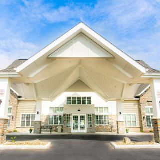 A grand entrance of a modern building with a large overhanging roof and multiple windows.
