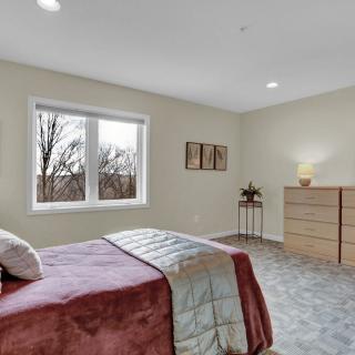 A minimalist bedroom with a bed, dresser, and window providing natural light.