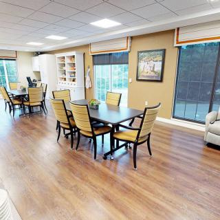 A spacious dining area with multiple tables and chairs, featuring large windows and a hardwood floor.