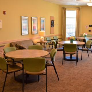 A cozy lounge area with tables, chairs, and a sofa arranged on a carpeted floor.
