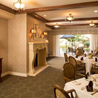 An elegant dining room with a fireplace, chandeliers, and neatly arranged tables and chairs.