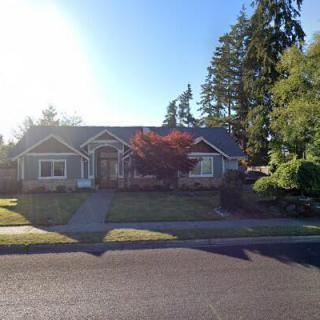 A suburban house surrounded by trees with sunlight casting shadows on the lawn.