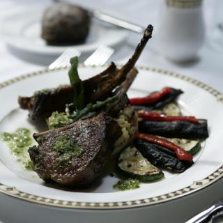 A gourmet dish featuring lamb chops served with asparagus, zucchini, and red peppers.