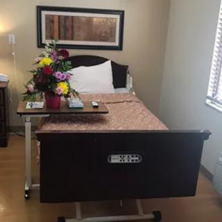 A hospital room with a neatly made bed and a bouquet of flowers on the bedside table.