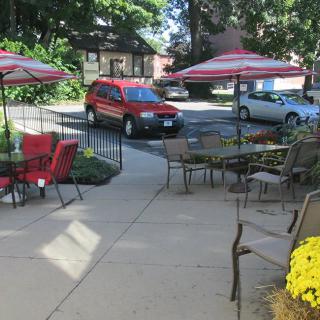 A cozy outdoor patio with tables, umbrellas, and a view of a red SUV parked nearby.