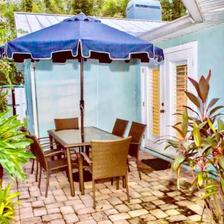 A cozy patio setup with a table, chairs, and an umbrella surrounded by lush plants.