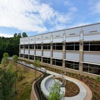 A modern building with large windows surrounded by landscaped greenery under a blue sky.
