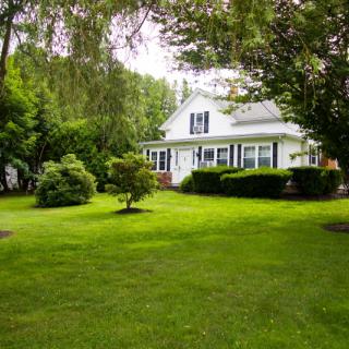 A charming white house surrounded by lush green lawn and trees.