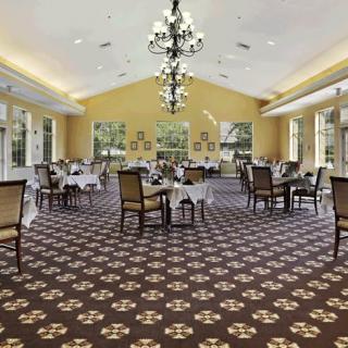 An elegant dining room with chandeliers, carpeted flooring, and neatly arranged tables and chairs.