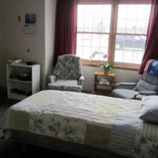 A cozy bedroom with a bed, armchairs, and natural light streaming through the window.