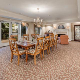 A spacious dining room featuring a long wooden table with matching chairs, adorned by an elegant chandelier and complemented by a patterned carpet.