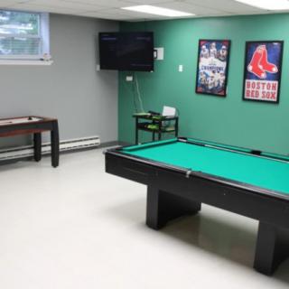 A game room featuring a billiards table, foosball table, and wall-mounted television with sports posters.