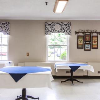 A well-lit dining area with tables covered in blue and white tablecloths, framed by patterned curtains and decorative wall hangings.