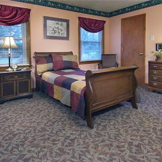 A traditional bedroom with a wooden bed, colorful quilt, and matching furniture.