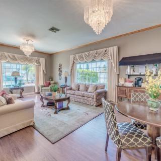 A spacious and elegantly decorated living room with chandeliers, comfortable sofas, and large windows adorned with decorative curtains.