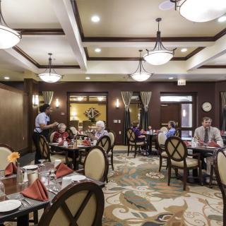 A formal dining area with people seated at tables and a waiter attending to guests.