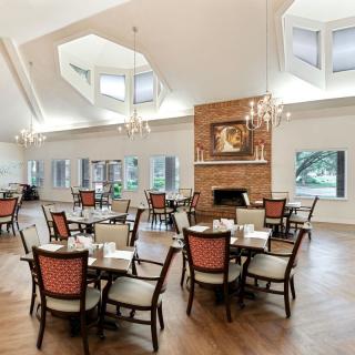 A spacious dining area with multiple tables and chairs, featuring a brick fireplace and large windows.