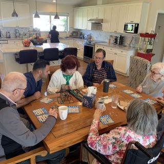 A group of seniors gathered around a table playing cards in a kitchen setting.