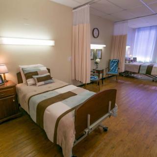 A clean and organized hospital room with a single bed, nightstand, and privacy curtains.