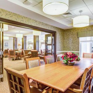 A spacious dining room with a wooden table, surrounded by chairs and adorned with a floral centerpiece under elegant lighting.