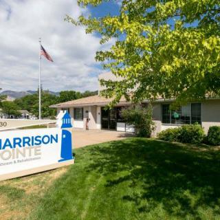 A view of the Harrison Pointe building with a sign, tree, and flag outside.