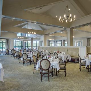 An elegant restaurant dining area with neatly arranged tables and chairs, illuminated by a chandelier.