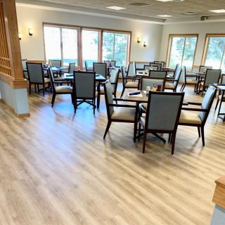 A bright and spacious dining room with multiple tables and chairs, featuring a wooden floor.