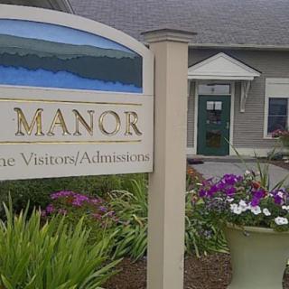 A sign for a manor with a landscaped entrance and flowers.