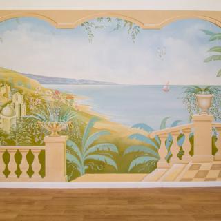 A mural depicting a scenic seaside view from a balcony with lush greenery.