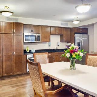 A modern kitchen and dining area featuring wood cabinets, a table with a floral centerpiece, and sleek appliances.