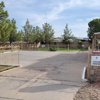 A fenced outdoor space with a parking lot and trees, indicating a residential area entrance.