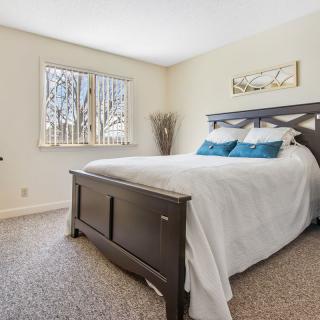 A modern bedroom with a large bed, white bedding, and decorative pillows, featuring a window that lets in natural light.