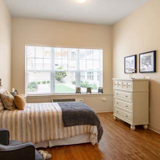 A cozy bedroom with a large window, bed, and dresser in a minimalist style.